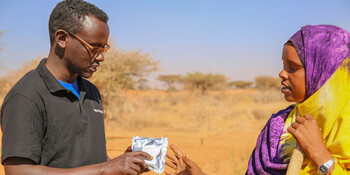 Ein Helfer gibt einer Landwirtin in Somalia dürreresistentes Saatgut