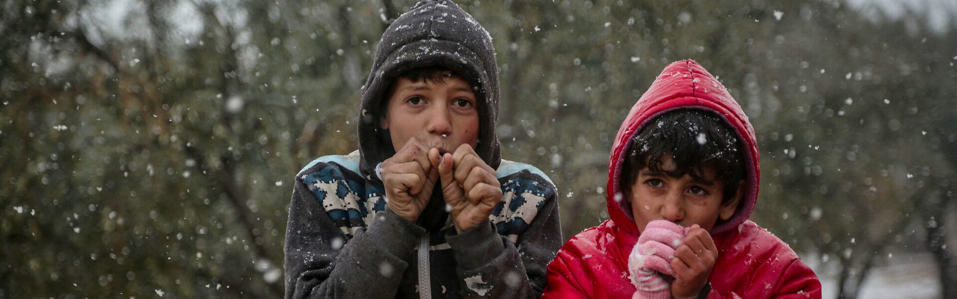 Zwei syrische Jungs in spärlicher Winterkleidung, die im Schnee frieren