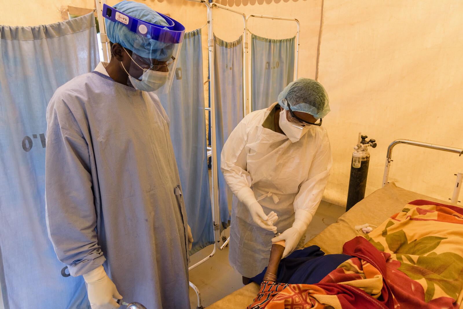 Ärzte mit Masken und Schutzanzügen legen bei einem Corona-Patienten in Tansania eine Infusion an