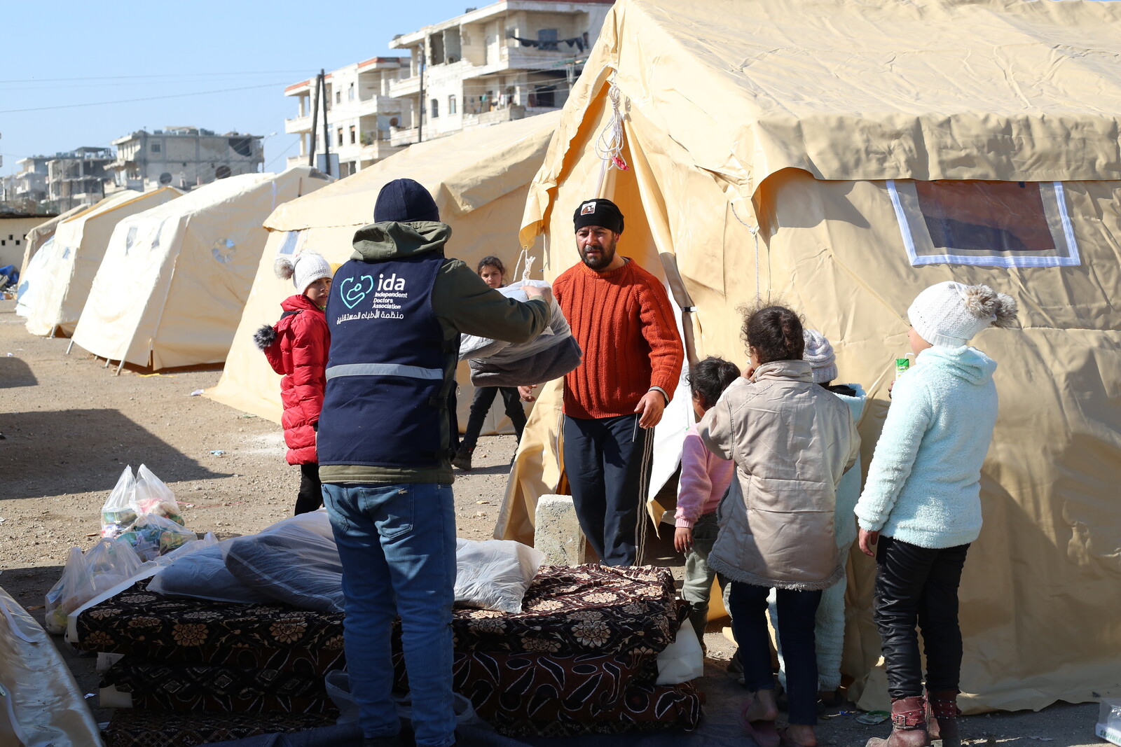 Ein Helfer übergibt Hilfsgüter wie Matratzen an Geflüchtete in Syrien