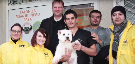 Mitarbeiter von Help vor einem serbischen Hundesalon. Der Besitzer hält ein Hund im Arm.