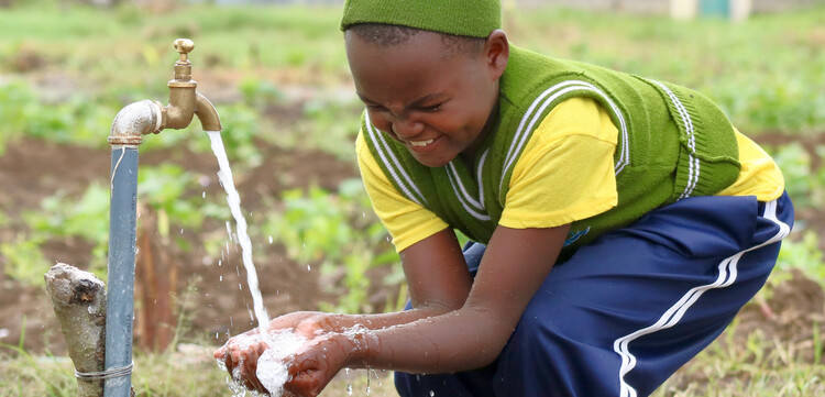 In Kenia freut sich ein Schulmädchen über das saubere Wasser, das aus dem Brunnen kommt