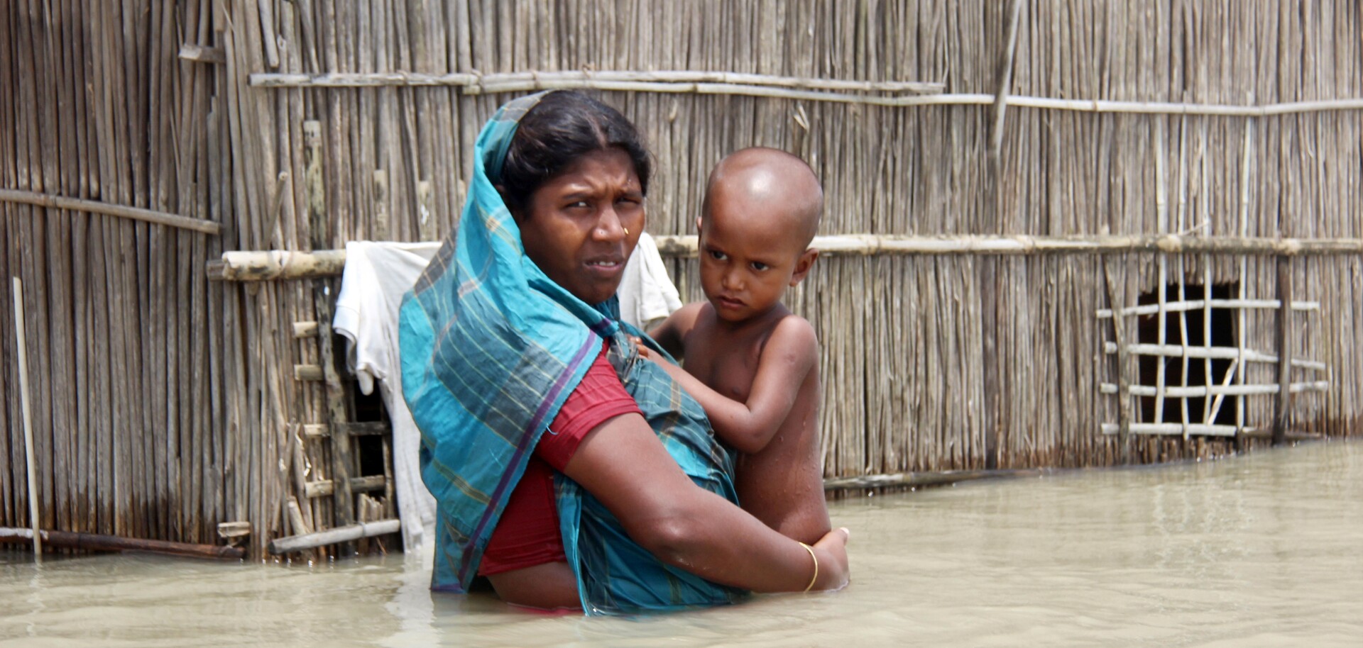 In einem Dorf in Bangladesch hält eine Mutter ihr Kind im Arm - mitten im Hochwasser In einem Dorf in Bangladesch hält eine Mutter ihr Kind im Arm - mitten im Hochwasser