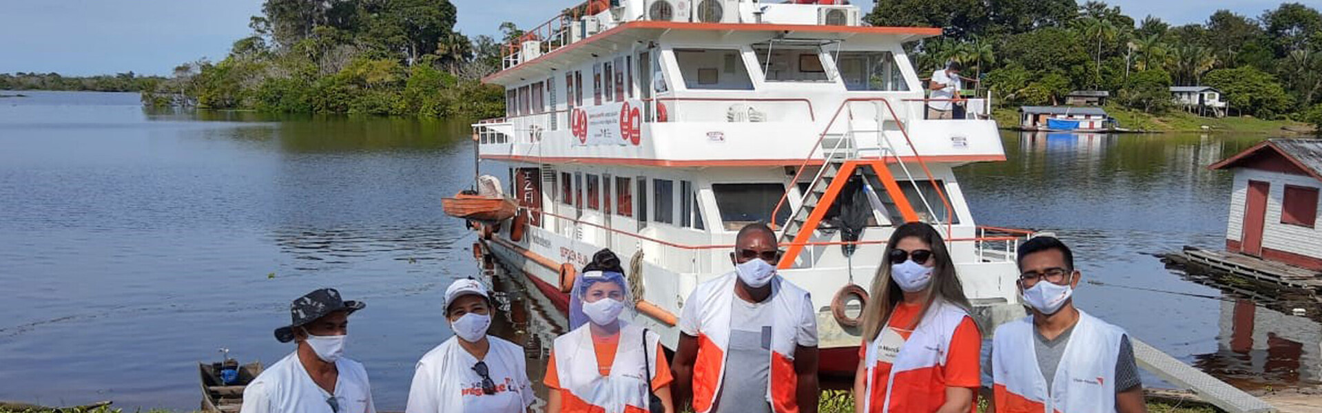 Helfer von World Vision stehen vor dem Schiff, das vom Corona-Virus betroffene Flussuferbewohner im Amazonas mit Medikamenten versorgt 