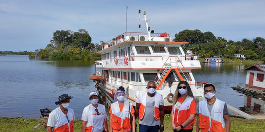 Helfer von World Vision stehen vor dem Schiff, das vom Corona-Virus betroffene Flussuferbewohner im Amazonas mit Medikamenten versorgt 