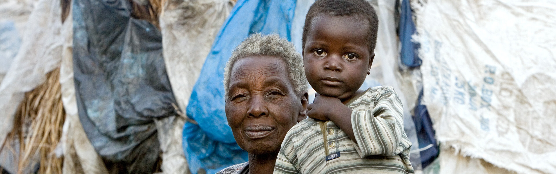 In der Demokratischen Republik Kongo herrscht eine unsichere Lage. Viele Menschen fliehen vor Gewalt und Krieg. Eine Oma sitzt mit ihrem Enkel in einem Flüchtlingslager.