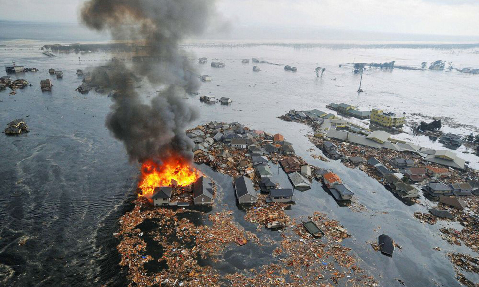 Vom Tsunami weggeschwemmte Häuser sind in Brand geraten. © REUTERS/KYODO Kyodo