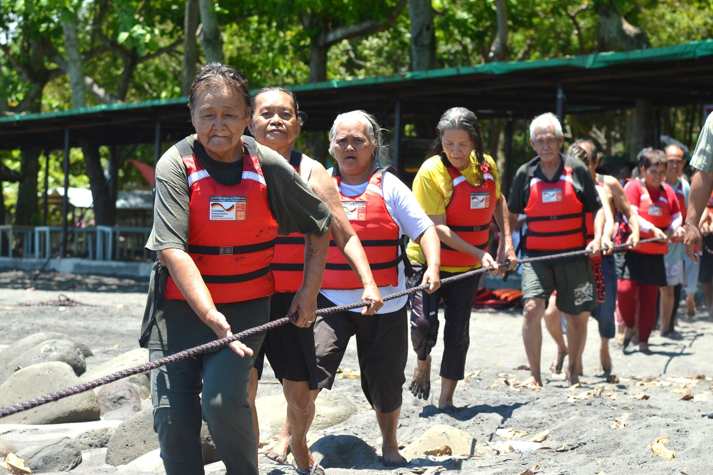 Eine Gruppe von Männern und Frauen mit Rettungsweste auf den Philippinen hangeln sich an einem Tau entlang Eine Gruppe von Männern und Frauen mit Rettungsweste auf den Philippinen hangeln sich an einem Tau entlang