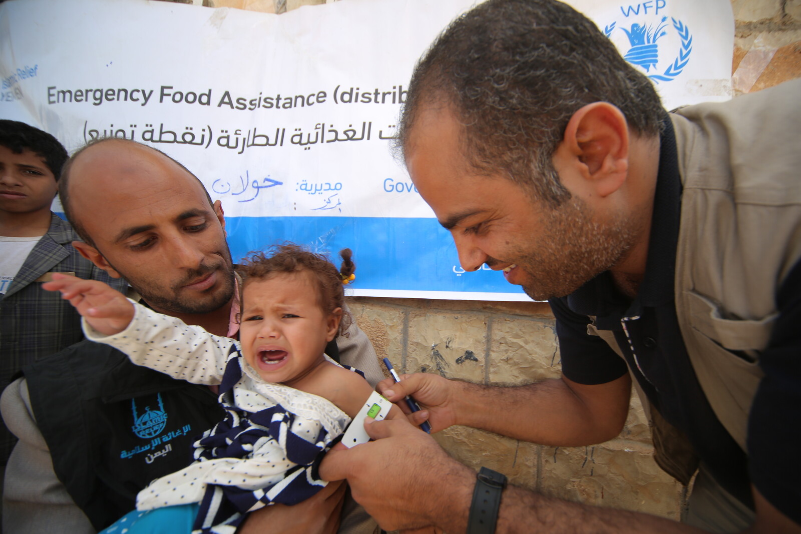 Im Jemen versorgt ein Mitarbeiter unserer Bündnisorganisation ein vor Hunger weinendes Kind