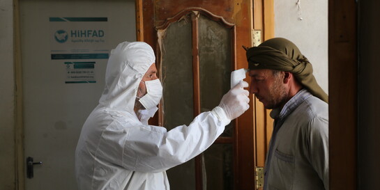 Ein Gesundheitshelfer im Schutzanzug und Mund-Nasen-Maske misst einem Mann an der Stirn Fieber
