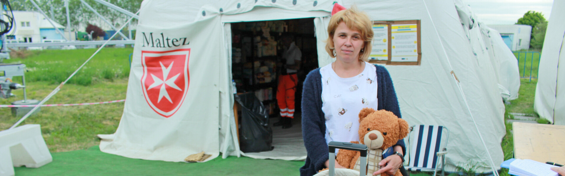 Eine vor dem Ukraine-Krieg geflüchtete Frau steht mit ihrem Koffer vor einem Zelt der Hilfsorganisation Malteser 