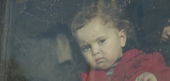 Ein syrisches Kind steht hinter einer Glasscheibe.