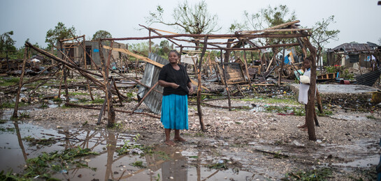 Eine Frau steht auf Haiti vor von Hurrikan Matthew zerstörten Hütten und Feldern.