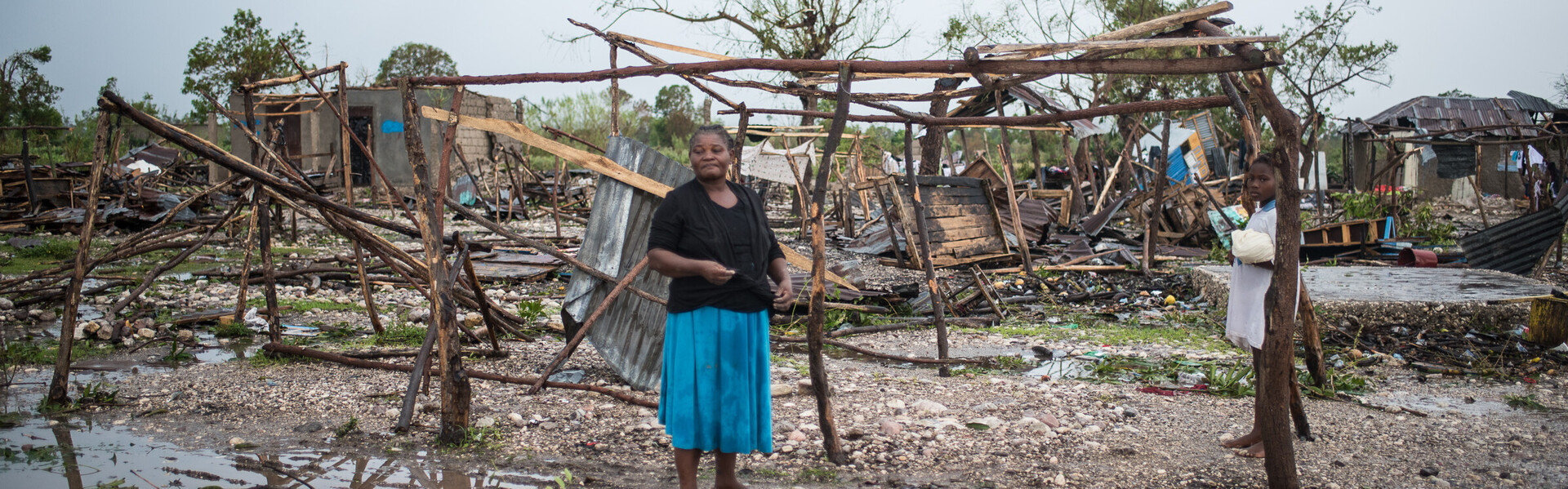 Eine Frau steht auf Haiti vor von Hurrikan Matthew zerstörten Hütten und Feldern.