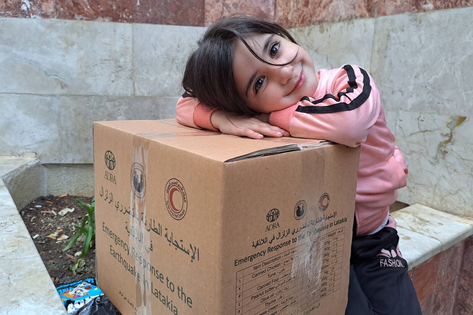 Ein Mädchen lehnt sich auf ein Hilfspaket in Syrien