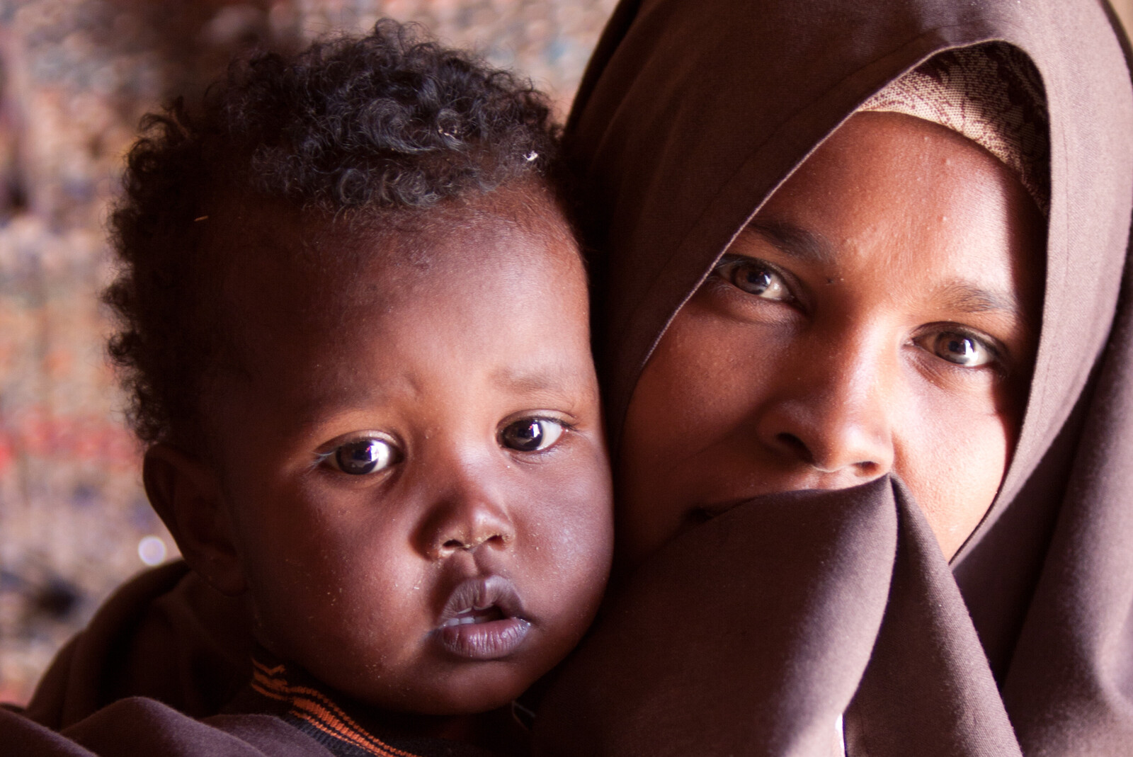 In Afrika herrscht oft Dürre und Hunger. Eine Frau mit ihrem Kind auf dem Arm sitzt in einem Zelt.