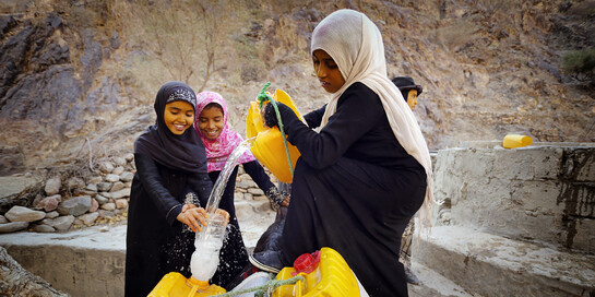 Drei Mädchen im Jemen füllen Wasser in gelbe Kanister um