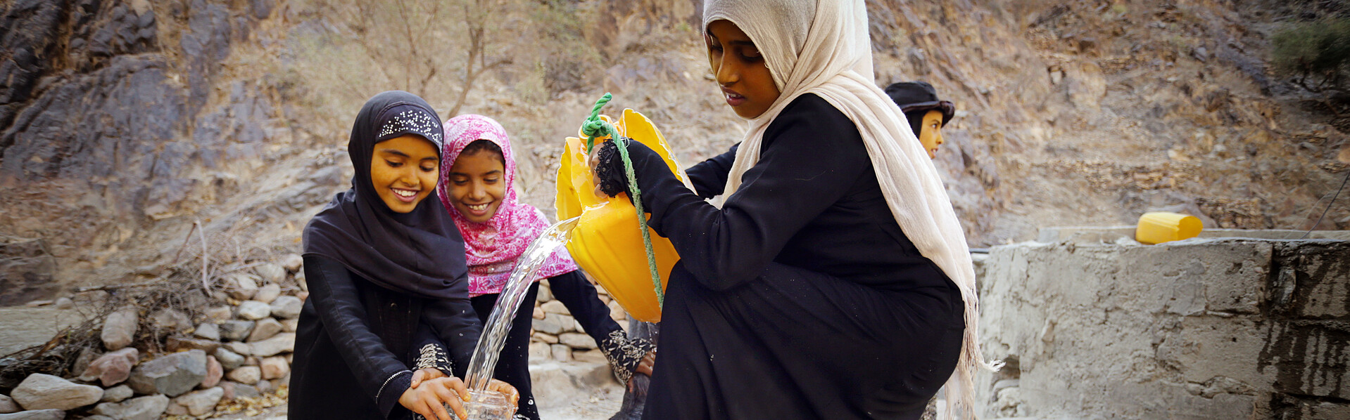 Drei Mädchen im Jemen füllen Trinkwasser in gelbe Kanister um Drei Mädchen im Jemen füllen Trinkwasser in gelbe Kanister um