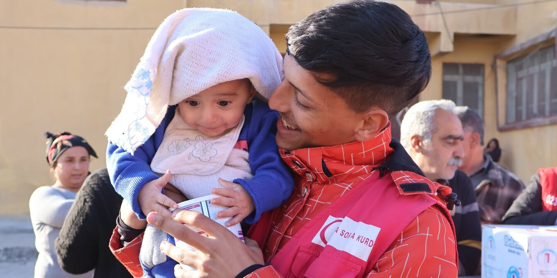 Ein humanitärer Helfer hält bei der Verteilung von Hilfsgütern ein Kind im Arm