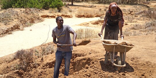 Ein Mann und eine Frau in Afrika bewirtschaften einen trockenen Ackerboden 