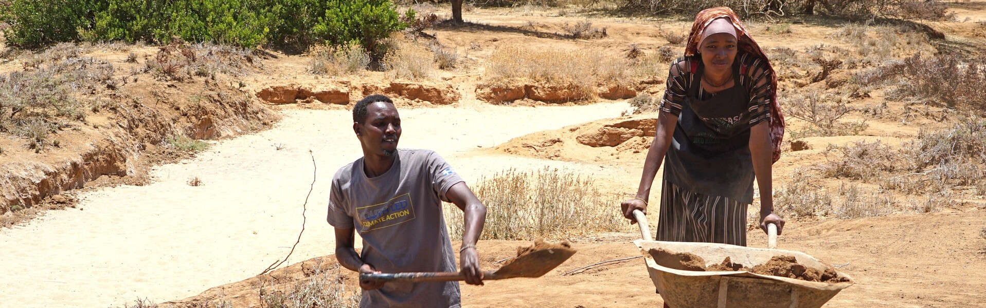 Ein Mann und eine Frau in Afrika bewirtschaften einen trockenen Ackerboden 