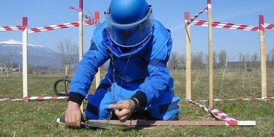 Ein Mann im Schutzanzug steckt ein Suchfeld zur Entminung ab