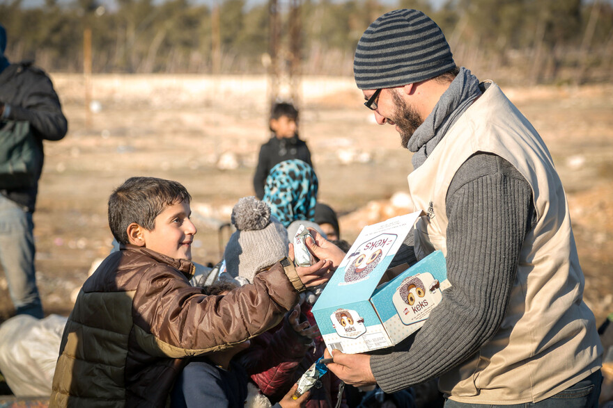 Ein Helfer verteilt in Syrien Nahrungsmittel an einen Jungen