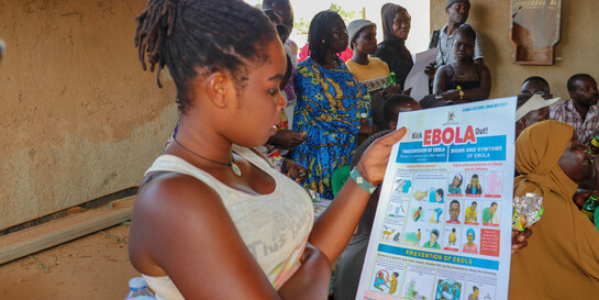 Eine Frau schaut sich ein Plakat an, auf dem Maßnahmen gegen Ebola-Übertragungen stehen