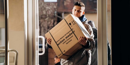 Ein Helfer trägt ein Paket mit Hilfslieferungen von der Organisation action medeor