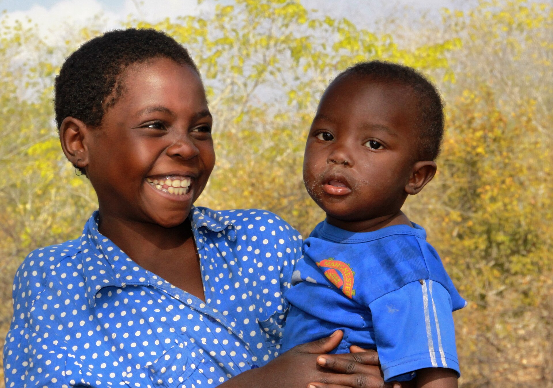 Ein Mädchen mit Kind lacht in Simbabwe während der Dürre- und Hungerkatastrophe durch die Auswirkungen von El Niño.