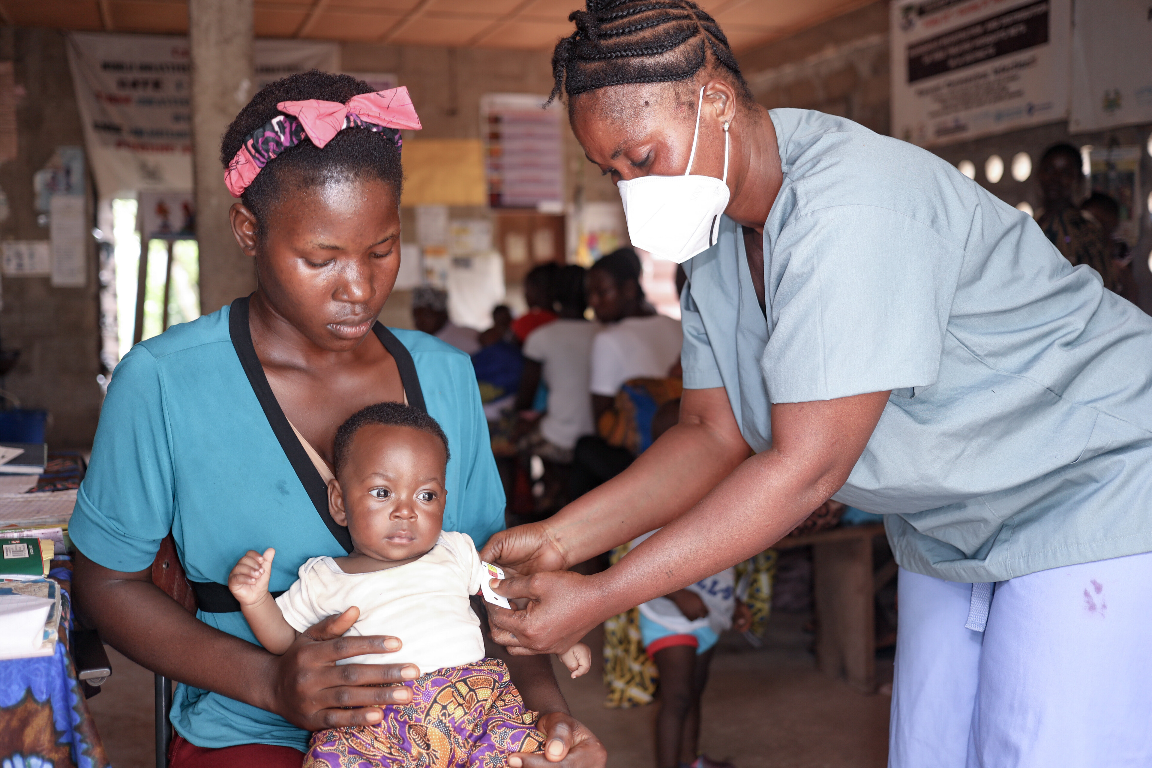 Ein Baby wird in Sierra Leone auf dem Schoß seiner Mutter von einer Helferin untersucht