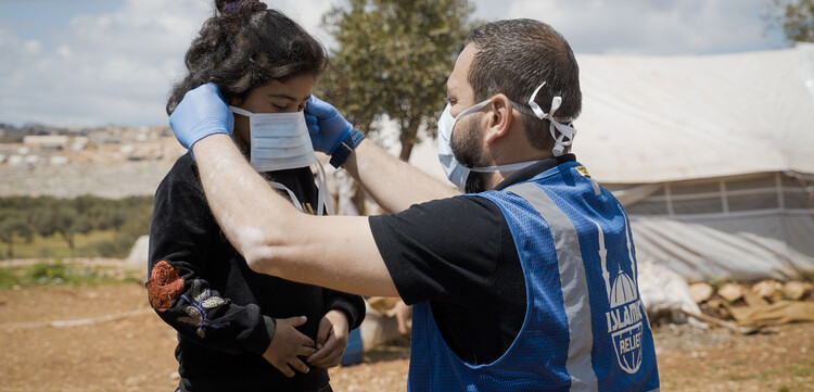Ein Helfer in Syrien bindet einem Mädchen eine Atemschutzmaske um