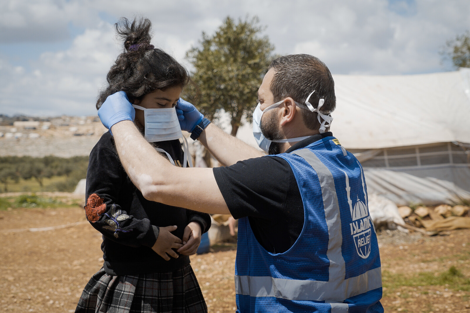 Ein Helfer in Syrien bindet einem Mädchen eine Atemschutzmaske um