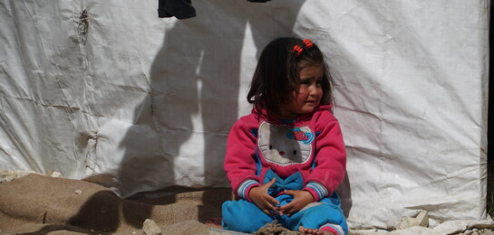 In Syrien sitzt ein Flüchtlingskind vor einem Vorhang.