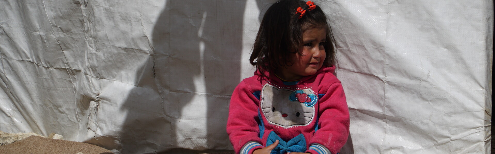 In Syrien sitzt ein Flüchtlingskind vor einem Vorhang.