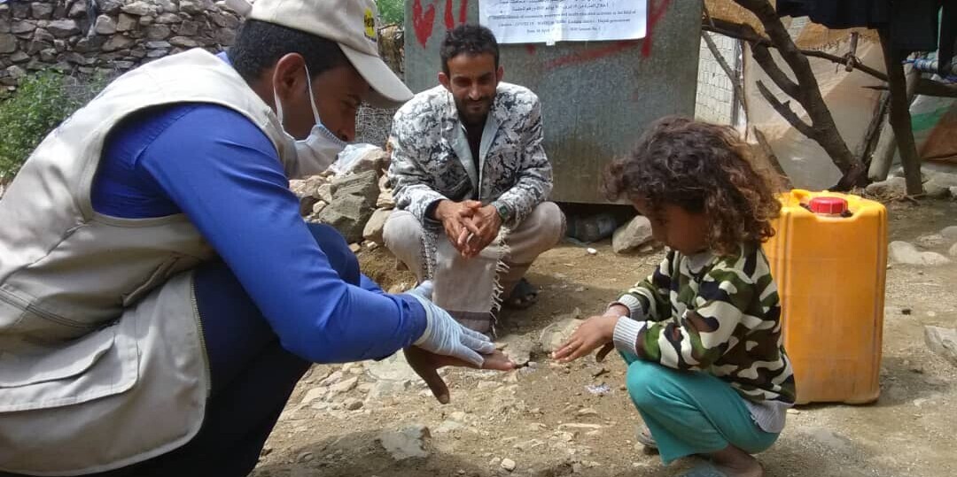 Ein Mitarbeiter von Help gibt einem Vater mit Kind eine Hygiene-Anleitung zur Vorbeugung von Cholera während der Corona-Pandemie Ein Mitarbeiter von Help gibt einem Vater mit Kind eine Hygiene-Anleitung zur Vorbeugung von Cholera während der Corona-Pandemie