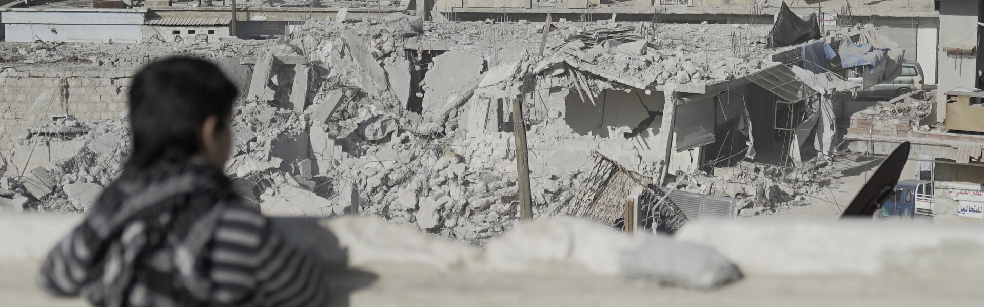 Ein Kind in Syrien blickt auf eine von Bomben zerstörte Stadt
