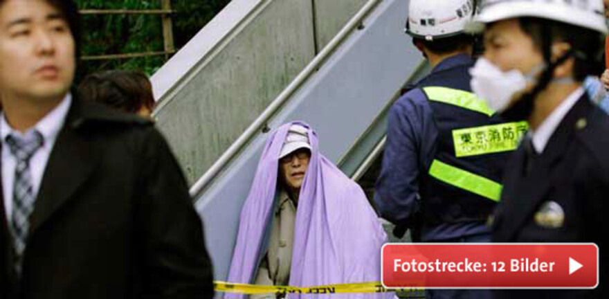 Im Finanzdistrikt Tokios sitzt ein Mann nach seiner Evakuierung in Decken gehüllt auf einer Treppe. © REUTERS/KYODO Kyodo