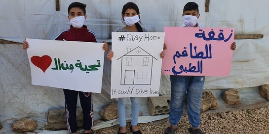 Drei syrische Kinder halten Schilder hoch ermutigen, während der Coronakrise zu Hause zu bleiben 