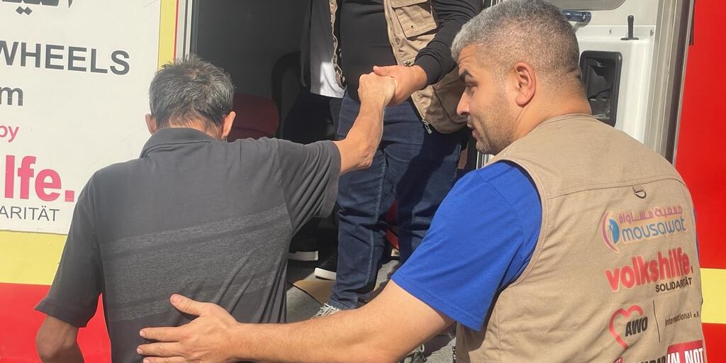 Zwei Helfer unterstützen einen älteren Mann im Libanon dabei, in eine mobile Gesundheitsstation zu steigen
