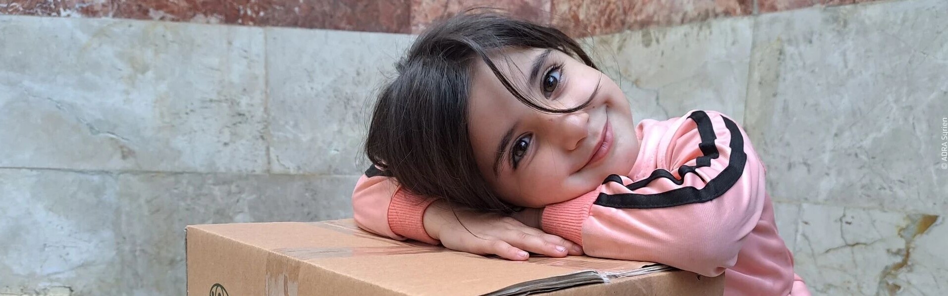 Mädchen aus Syrien freut sich über Hilfspaket