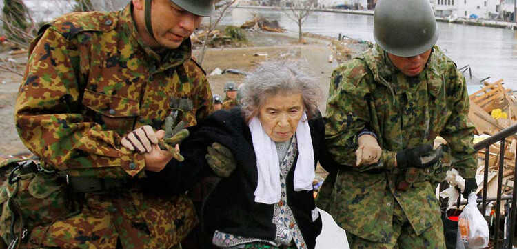 Soldaten bringen eine alte Frau in Sicherheit, die in einem von der Umwelt abgeschlossenen Rettungszentrum ausgeharrt hat.