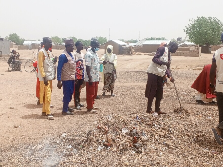 Ein Helfer zeigt Menschen in Nigeria Umwelthygienemaßnahmen, um die Umgebung sauber zu halten