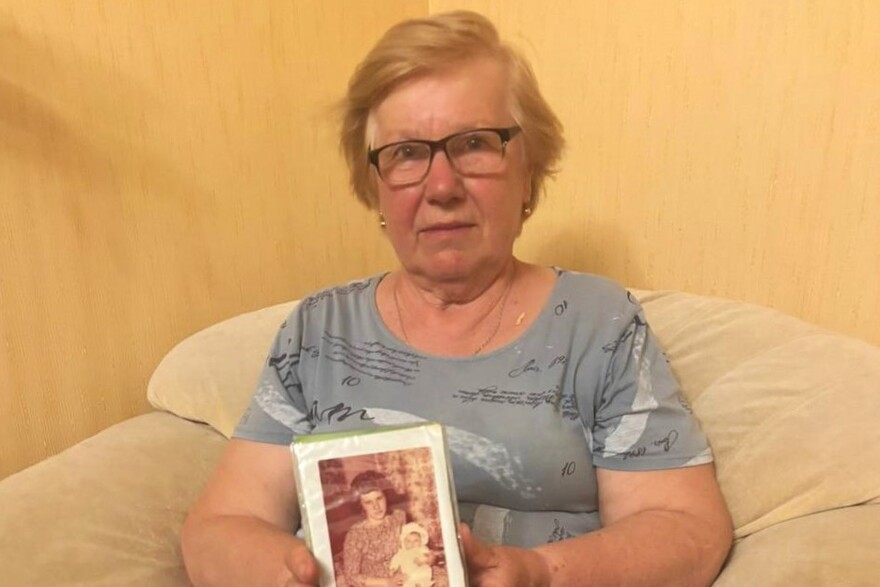Eine ältere Frau hält ein Fotoalbum in den Händen, auf dem eine Frau mit Kind zu sehen ist