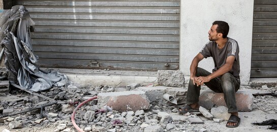 Flüchtlinge Syrien: Ein Mann sitzt mitten in einer von Krieg und Zerstörung betroffenen Straße. 