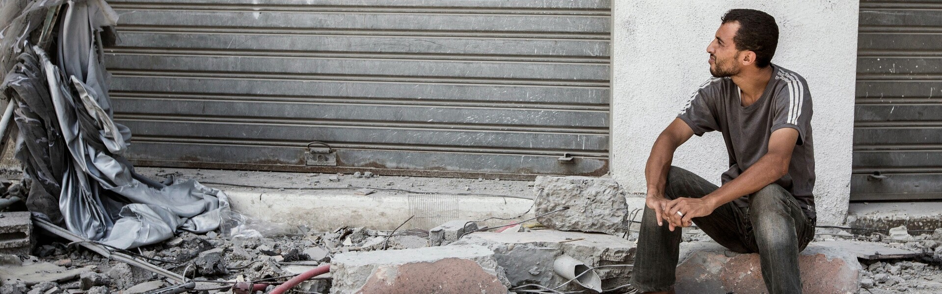 Flüchtlinge Syrien: Ein Mann sitzt mitten in einer von Krieg und Zerstörung betroffenen Straße. 