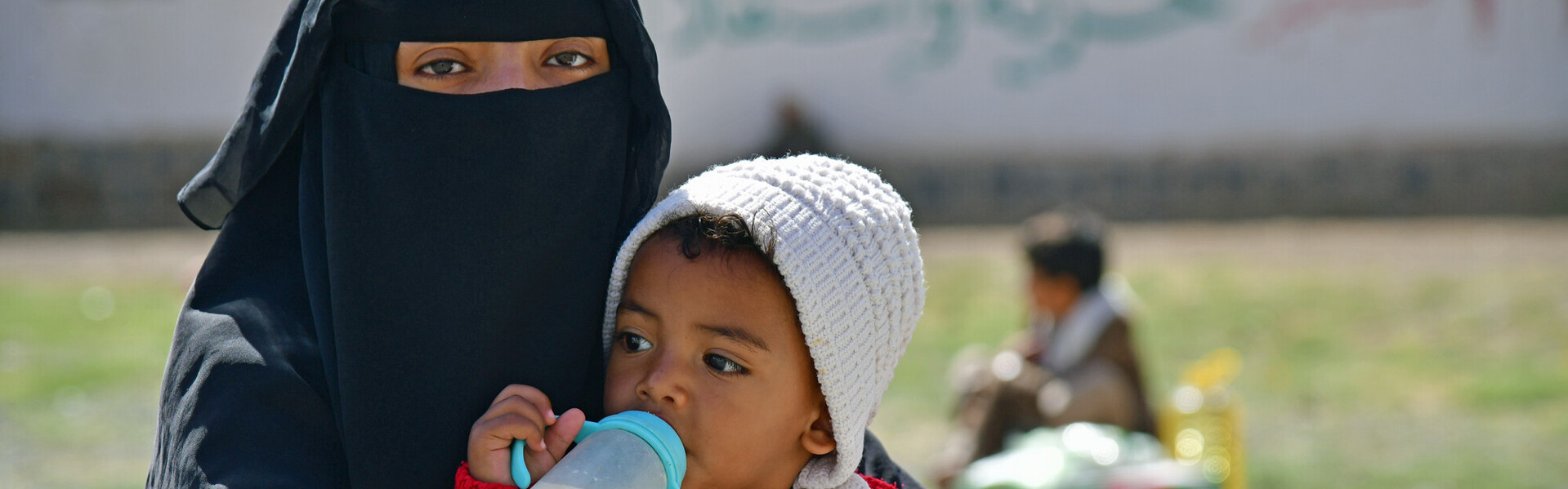Eine Frau mit schwarzem Nikab trägt ein Baby mit Milchflasche
