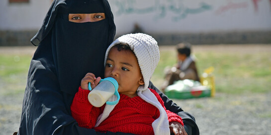 Eine Frau mit schwarzem Nikab trägt ein Baby mit Milchflasche