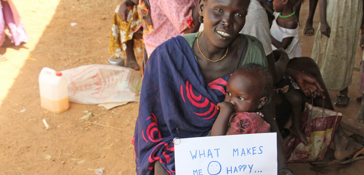 Eine Frau hält ihr Kind im Arm und einen Zettel mit der Aufschrift "What makes me happy - my child survived"