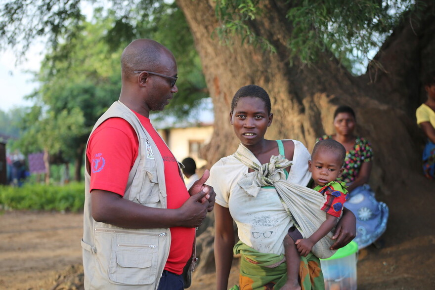 Ein Helfer spricht mit einer Mutter in Malawi, die ihr Kind auf dem Arm hält